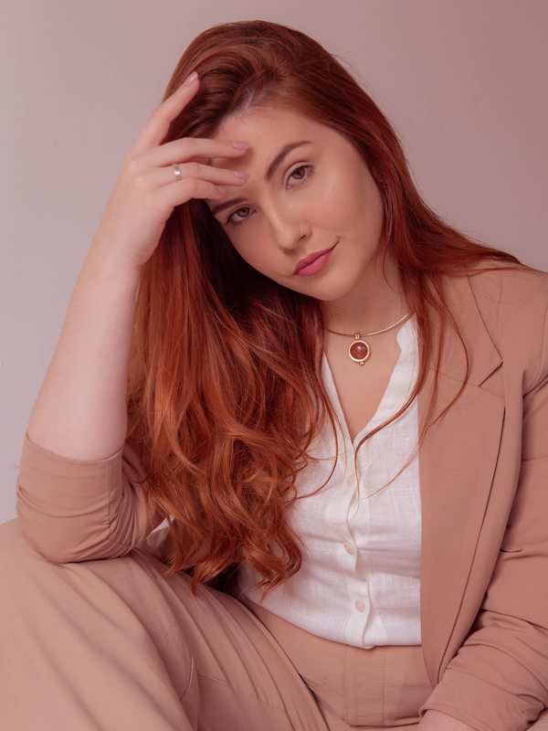 Duda sentada, de blazer bege, com a mão no cabelo